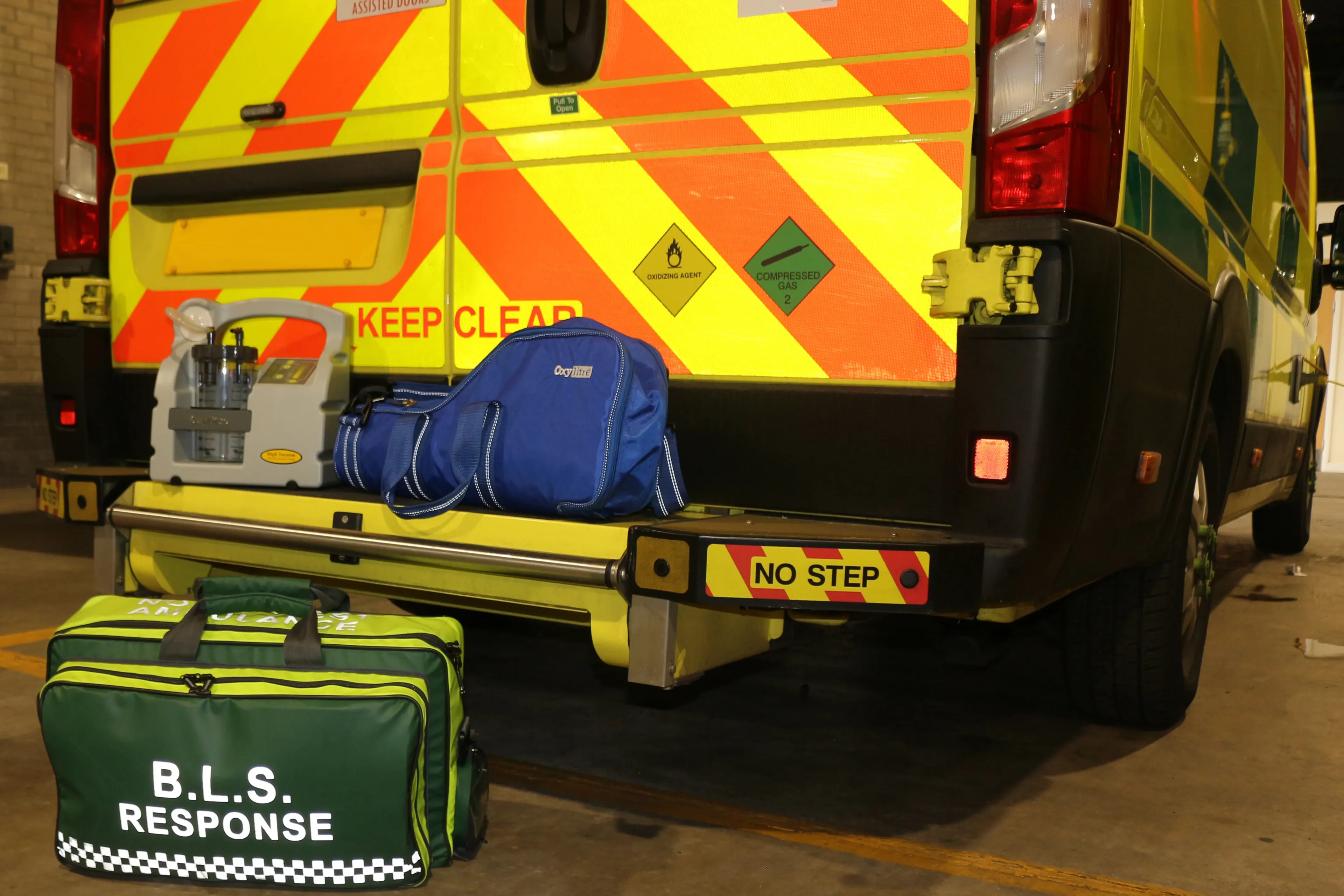 Oxylitre portable suction pump and blue equipment carry bag on the tail lift of an ambulance, with green response bags on the floor